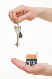 男人的手拿着一串钥匙和一个玩具房子