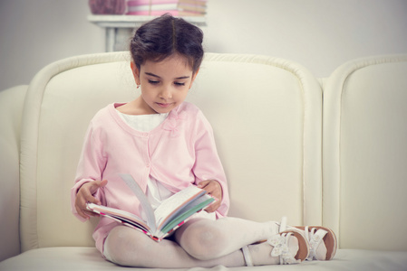 可爱的西班牙裔小女孩读本书在沙发上