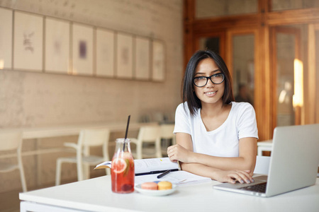 年轻的亚洲企业家学生在图书馆或开放空间咖啡馆看着镜头微笑的笔记本电脑上工作