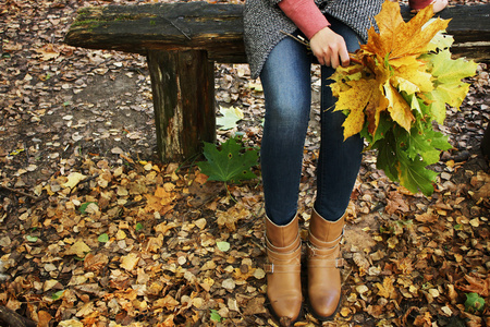 年轻漂亮的女孩坐在公园的长椅上，抱着一束堕落的枫树叶