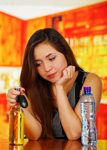 一个美丽的醉酒女人假扮她的手在她的下巴，用一瓶啤酒和水和托车钥匙在木桌上，在酒吧背景的肖像