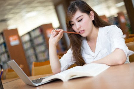 女留学生在图书馆与笔记本电脑