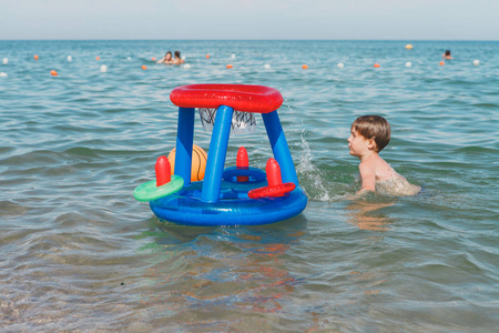 一个男孩在海边戏水充气的球上.打篮球在水中的小男孩插画