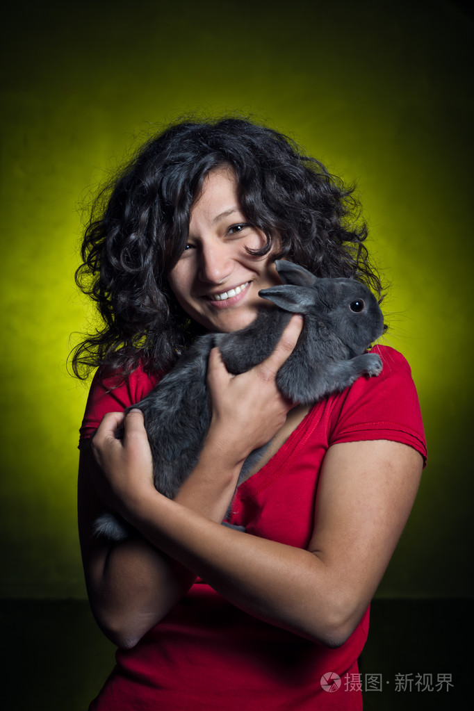 美丽的女孩抱着一只灰色的兔子