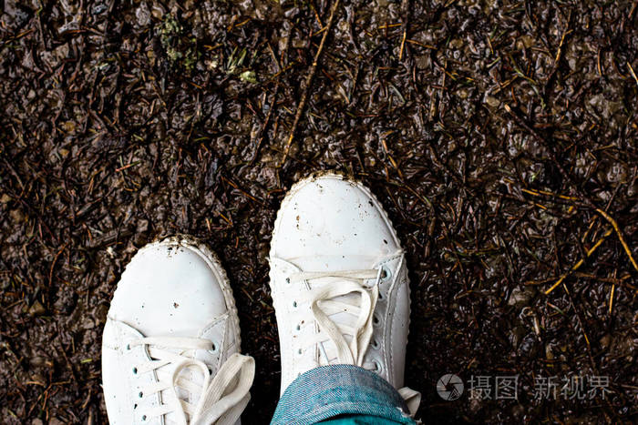 在白色运动鞋的妇女的腿站在泥地里秋泥