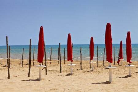 红色的封闭遮阳伞和木棍在地中海沙滩，西西里岛，在阳光灿烂的夏天一天