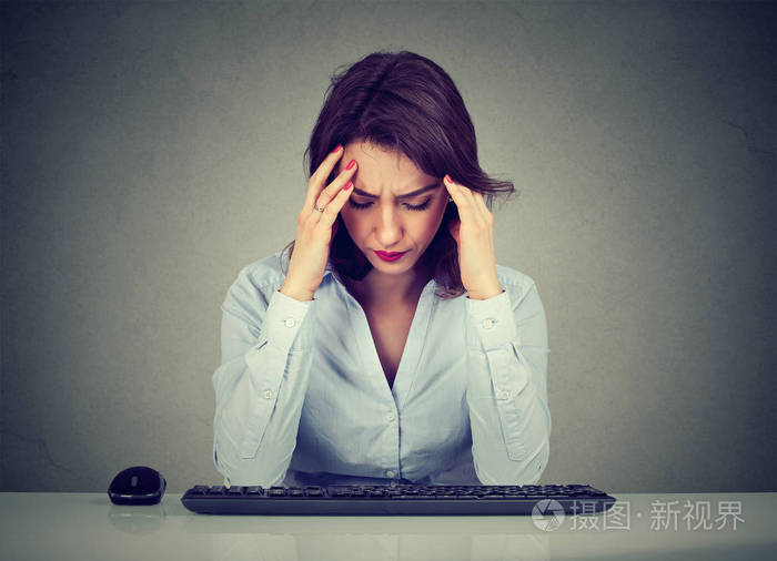 悲伤的女人坐在桌旁低头看电脑键盘