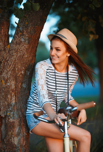 可爱的年轻女子在一辆自行车在户外一顶帽子