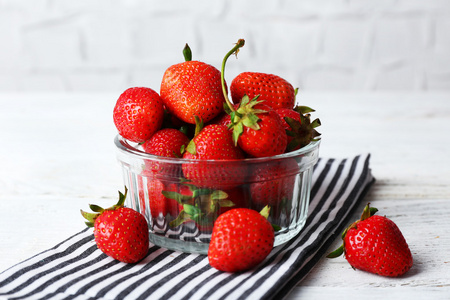 成熟的草莓在玻璃碟上餐巾放在木桌前，特写