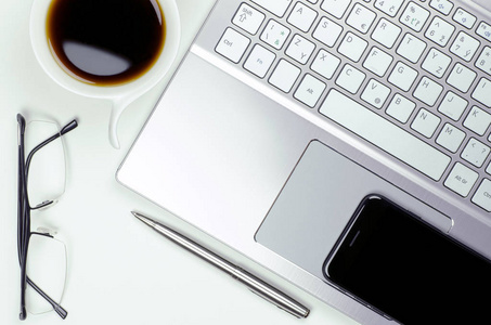 在白色背景上的静物与手提电脑和智能手机 笔和眼镜旁边一杯的咖啡特写视图