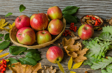 在秋天的落叶和旧木板背景上的柳条篮子里的苹果