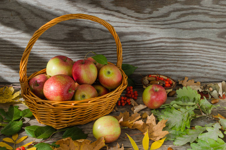 在秋天的落叶和旧木板背景上的柳条篮子里的苹果