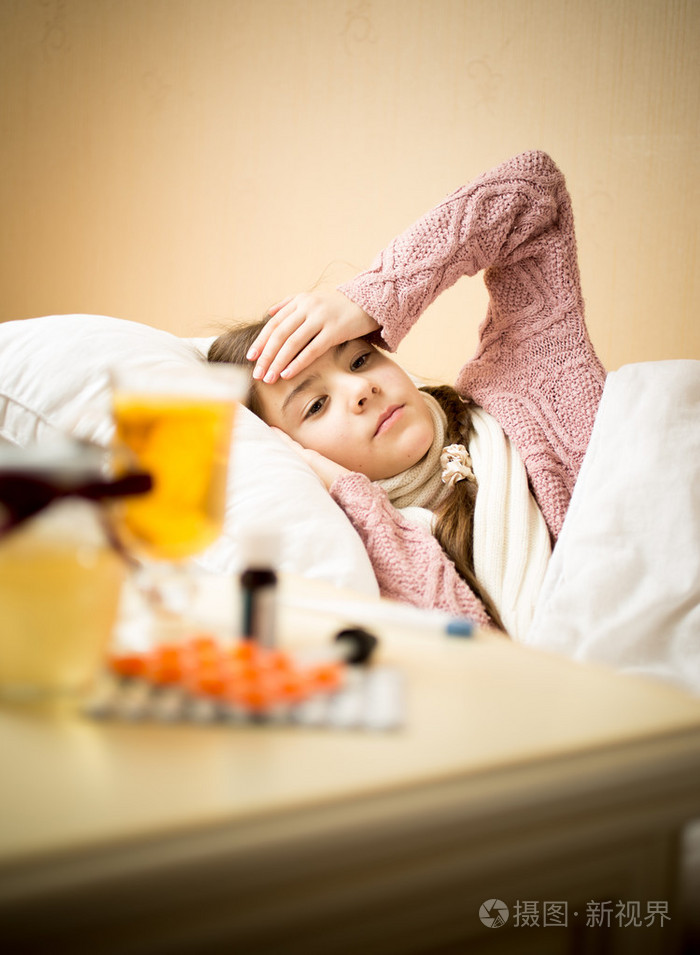 躺在桌子旁边的生病的女孩拿着药躺在床上