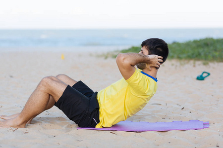 体育与健康的生活方式。年轻人做仰卧起坐海洋沙滩上