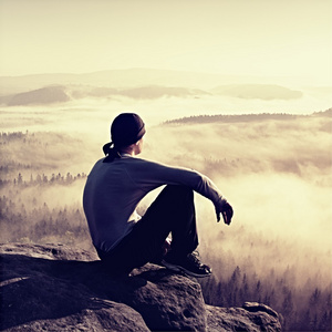 男人坐在岩石和观看到多彩雾，雾中森林谷峰