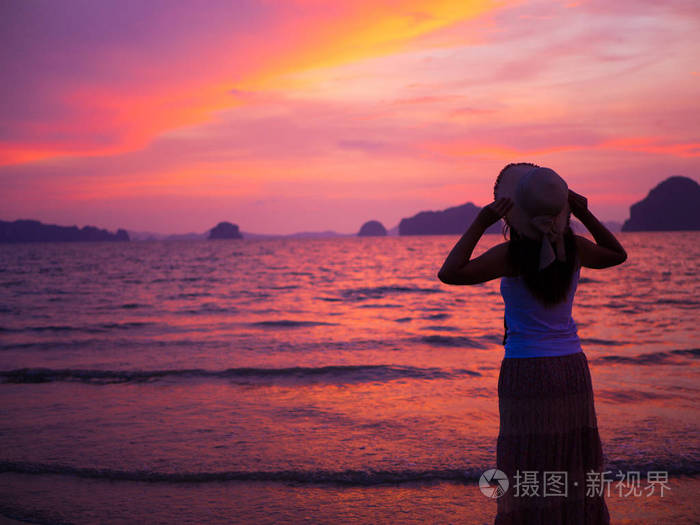 女人在海边戴着顶帽子下日出的张开双臂的轮廓夏天的概念