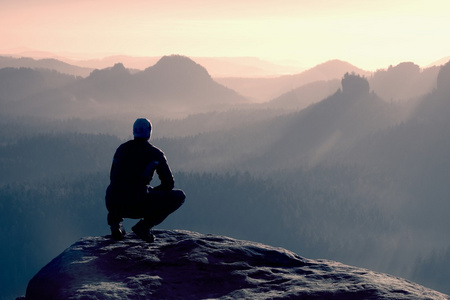 在黑色运动装的年轻男子是坐在悬崖的边上，期待迷雾笼罩的山谷贝娄