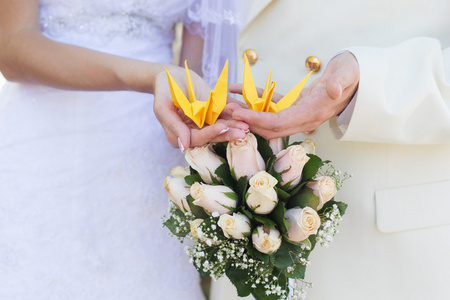 新娘和新郎的手拿着黄色的折纸鸟