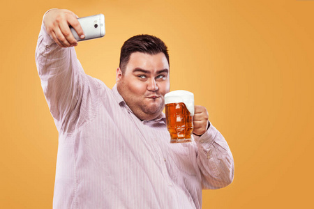 年轻的胖男人在慕尼黑啤酒节啤酒自拍照照片制作在智能手机上的黄色背景上