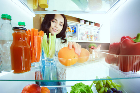 女性站附近打开冰箱充分的健康食品，蔬菜和水果的画像。女性肖像