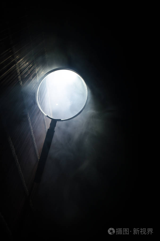 关闭了单带的放大镜黑处理靠在木头桌上橘红色烟雾暗背景上超现实背景