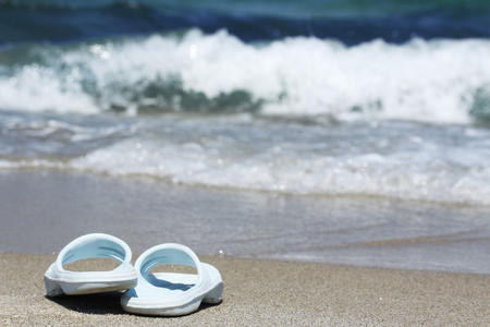 在沙滩在海浪上的蓝色拖鞋