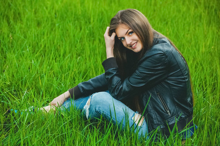 有吸引力的年轻的金发女孩，穿着一件灰色的外套和牛仔裤坐在草地上