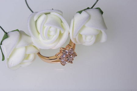 庆祝的的装饰品。用石头和束人造花的金戒指。米色白色背景上的玫瑰