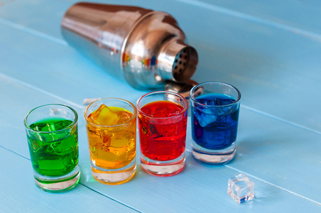 蓝色，黄色，绿色，红色酒精或无酒精的鸡尾酒，冰块和振动筛栏上的计数器 木制背景