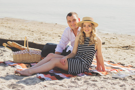 春光乍泄。水平的射击的美丽和年轻夫妇期待着相机和微笑着坐在海滩上野餐