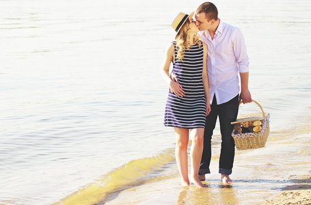 浪漫的散步。水平的年轻人亲吻他漂亮的女朋友，在海滩上散步，一起牵手保持篮子的射击