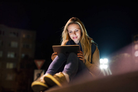 女人在城市在晚上举行平板电脑阅读的东西