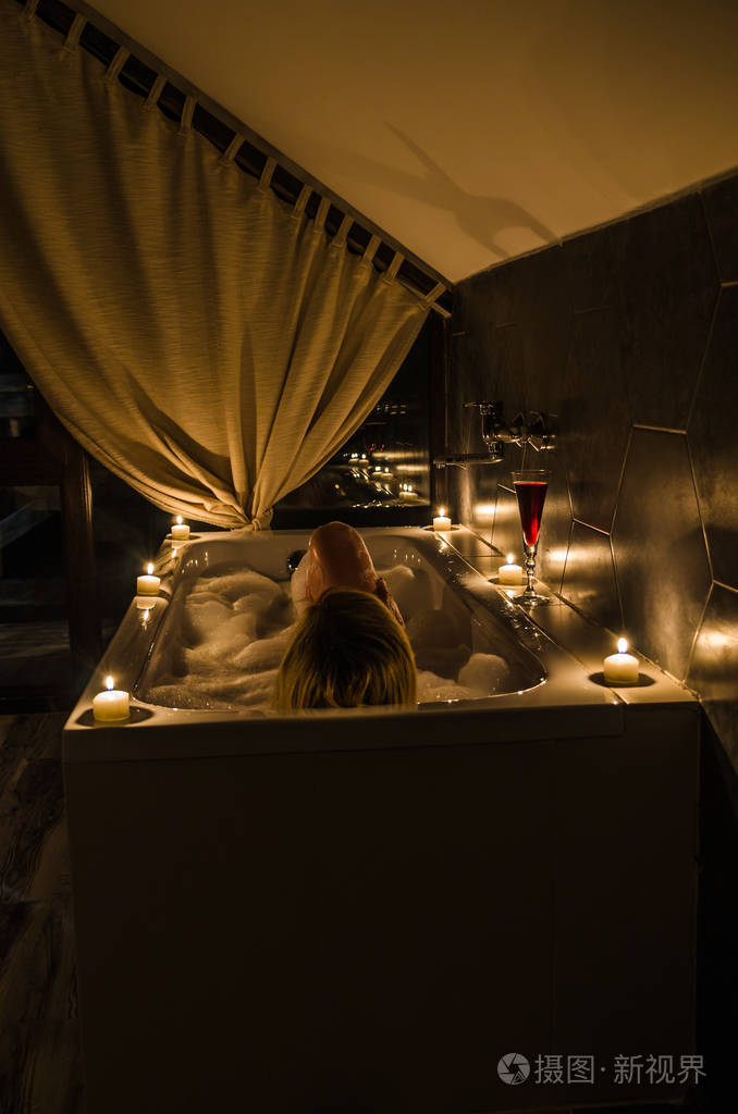 年轻的女孩在浴室里用蜡烛和红酒