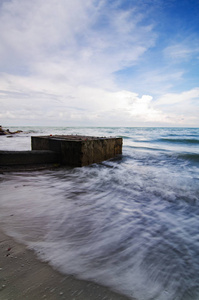 软的雪白浪花打在沙滩上的混凝土结构。由于长时间曝光 shot.soft 和蓝蓝的天空白云戏剧性的模糊的图像