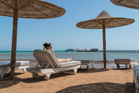 在海滩上的躺椅上晒日光浴的女孩。在后台一个码头是可见
