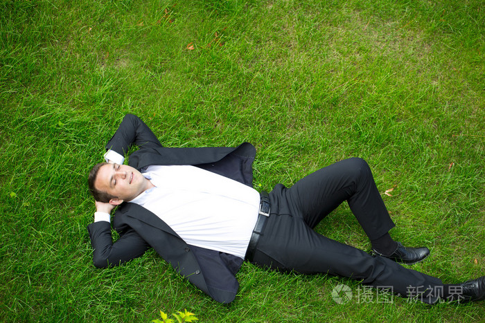 年轻的商人在一件西装躺在草地上查看从上面
