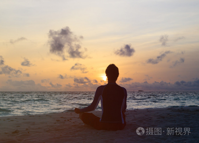 男人在日落海滩冥想的剪影