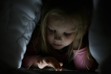小女孩晚上毯子从她的父母秘密在平板电脑上玩。