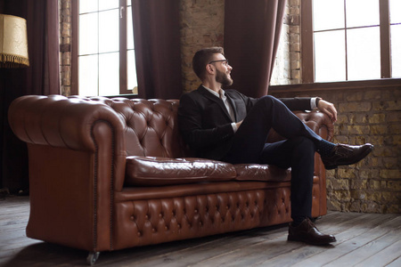 英俊的时尚自信胡子商人在一个聪明的西装和眼镜坐在沙发上办公室照片