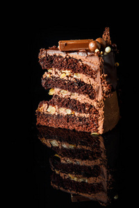 在黑色镜子背景下, 用巧克力糖果装饰的奶油夹层的一块美味巧克力蛋糕的垂直视图