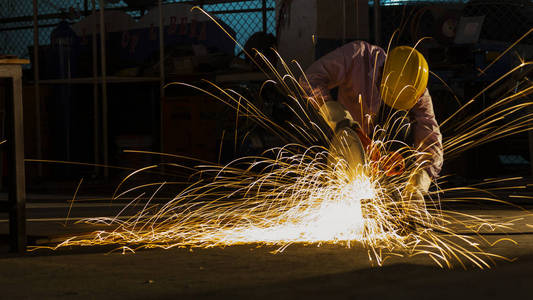 该工作人员使用切割机切割金属,专注于闪存浅色系的锋利的火花,在低光