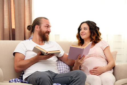 幸福的心爱夫妇读书在等待宝宝的诞生在房间里的沙发上
