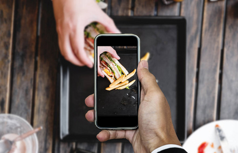 以食物照片，通过智能手机，俱乐部三明治配薯条木制的桌子上的食物摄影