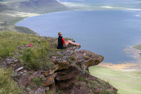 一名妇女坐在悬崖边山和湖的背景