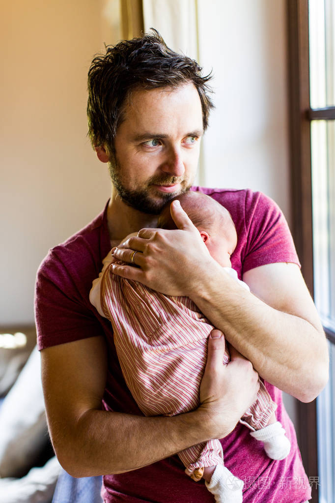 年轻的父亲在家里抱着他刚出生的婴儿的女孩照片-正版商用图片0d5h3m