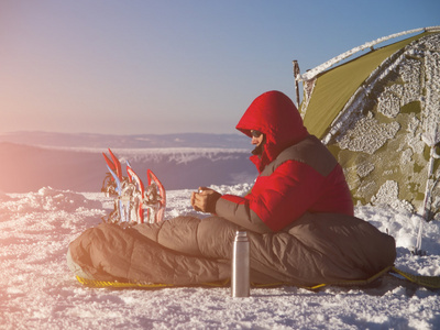 一个男人坐在睡袋里附近的帐篷和雪