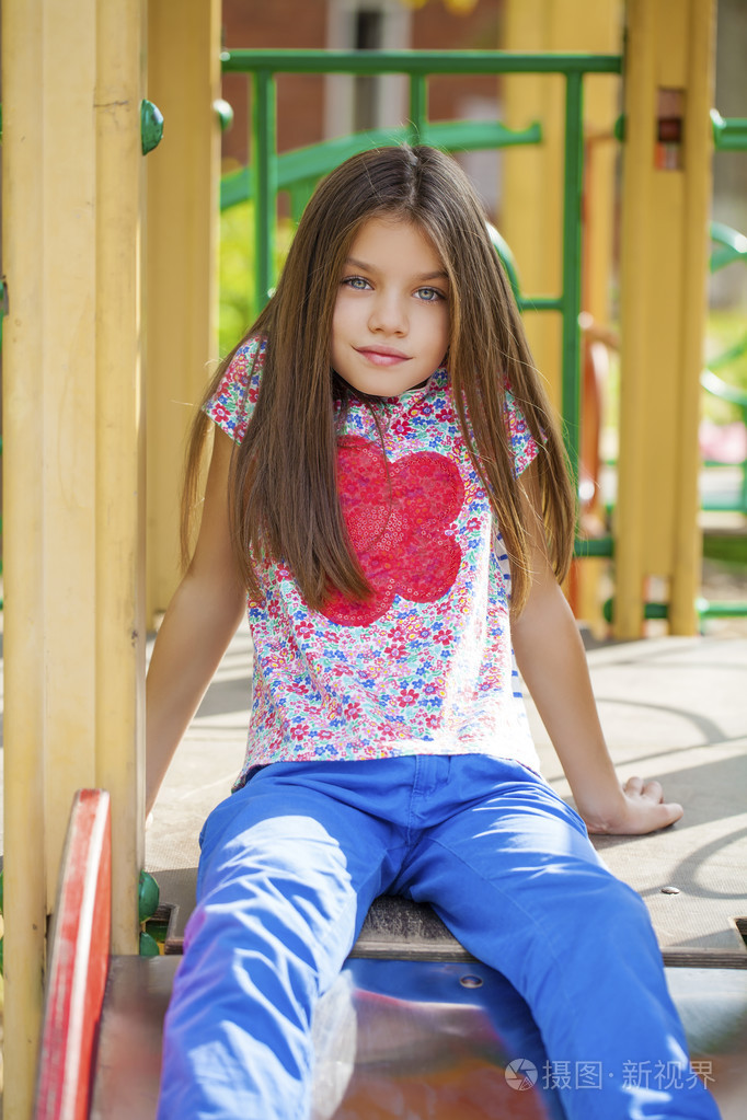 漂亮的小女孩在夏天城市公园的绿色背景上