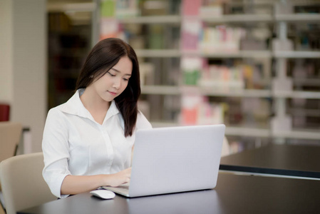 一个快乐美丽的亚洲学生的肖像在图书馆使用笔记本电脑