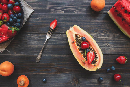 夏天的水果。新鲜多汁的浆果 西瓜和木瓜在黑色的木桌子，顶视图
