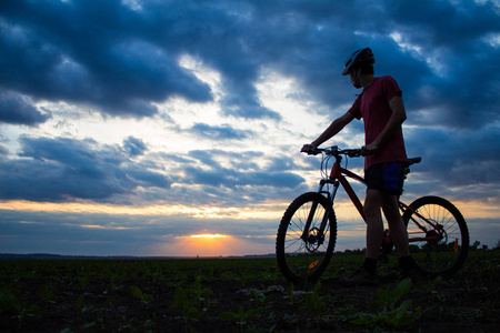 用一辆自行车在夕阳的天空以戏剧性的云时，现场一个年轻男人的轮廓